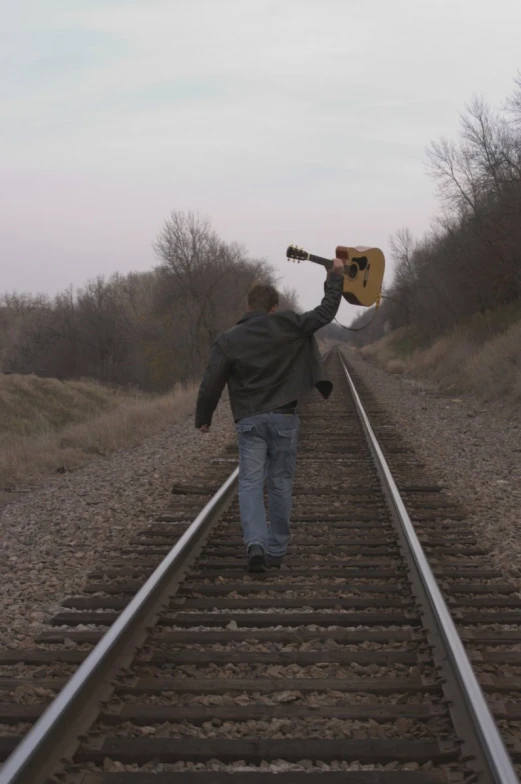 a man carrying a guitar over his shoulder and walking along the railroad tracks