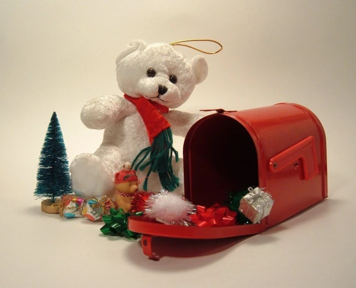 a white teddy bear in a red mailbox next to christmas trees