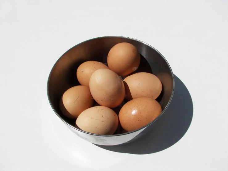 a silver bowl of brown eggs on top of a table