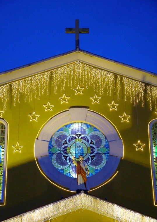 church with lighted facade displaying cross and religious stained glass window
