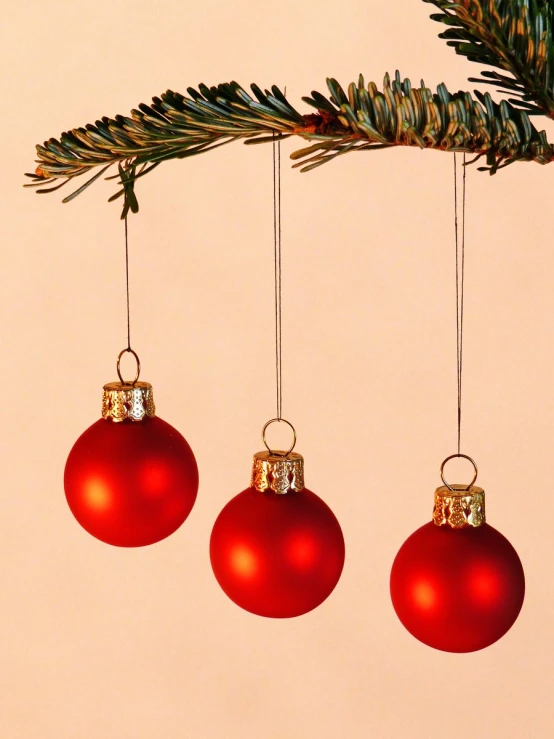 three red ornaments hanging from a christmas tree