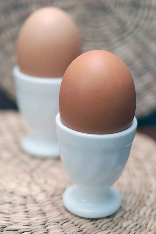 two eggs in white bowls on a wicker table