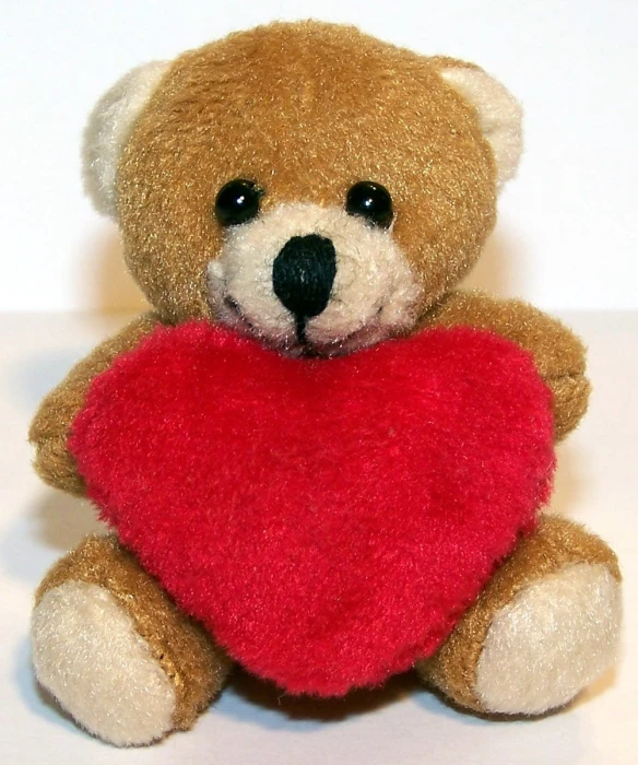 a small teddy bear holding a heart on white table