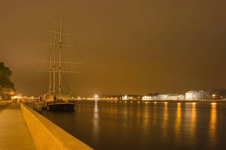 a large sail ship docked in the harbor of a city at night