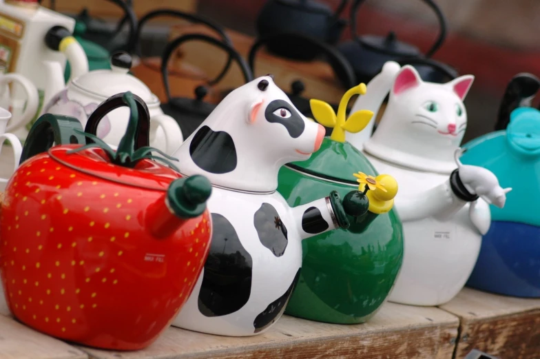 a row of ceramic teapots with the faces of cats holding strawberries