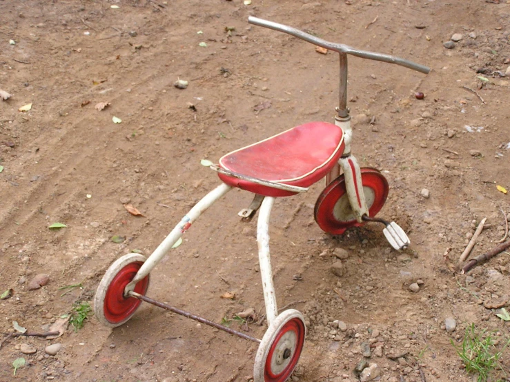 an old red tricycle that is on a dirty ground