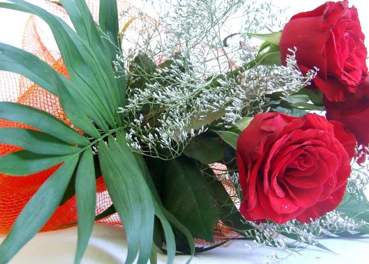 a bouquet of red roses and greenery on the table