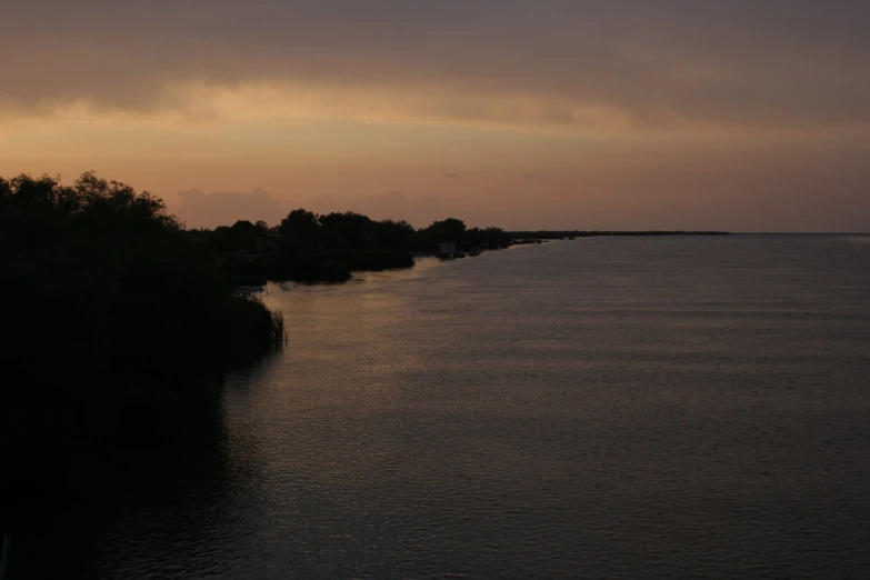 the sun is setting over the ocean and there are trees in the water