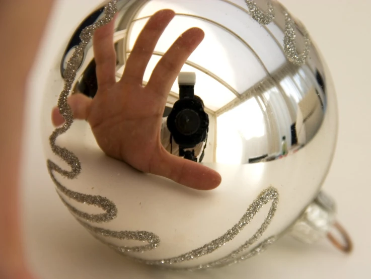 the reflection of a hand on a ball in a glass ornament