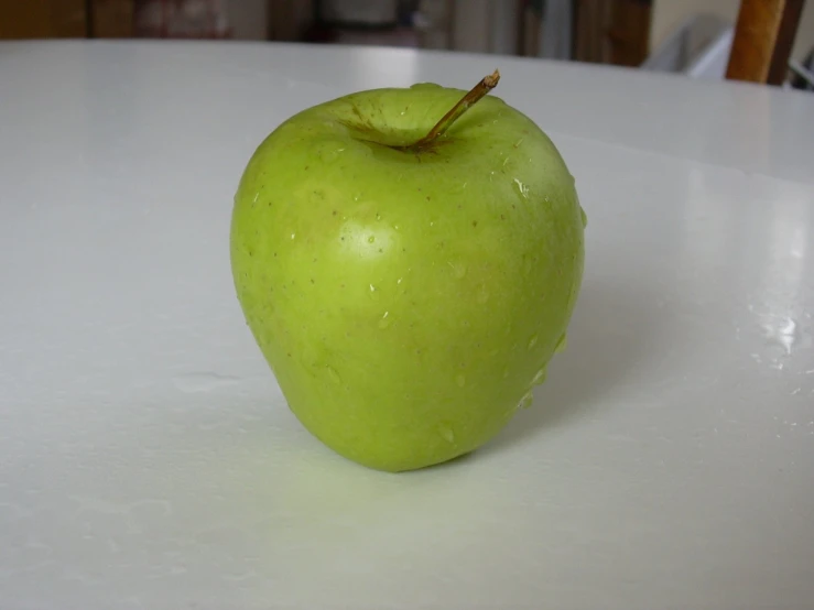 a green apple is sitting on a white table