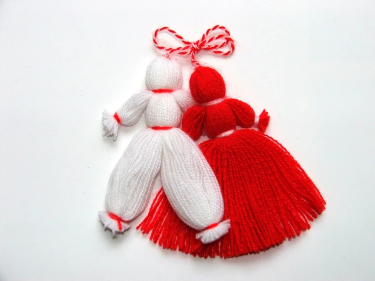 two knitted dolls in red and white outfits sitting on top of a white surface