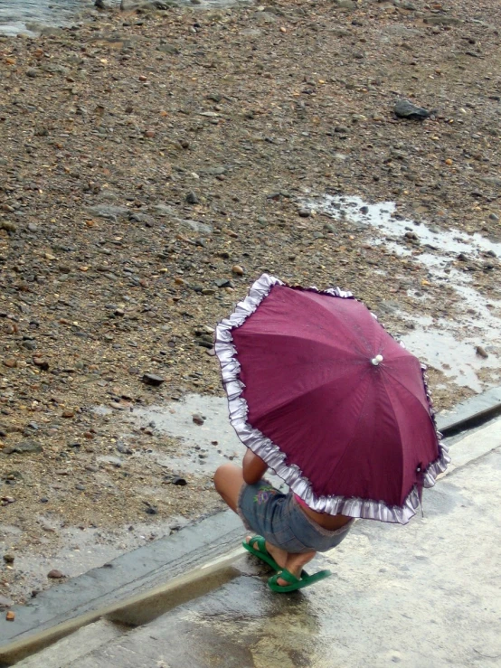 child wearing rain boots and umbrella in dle next to river