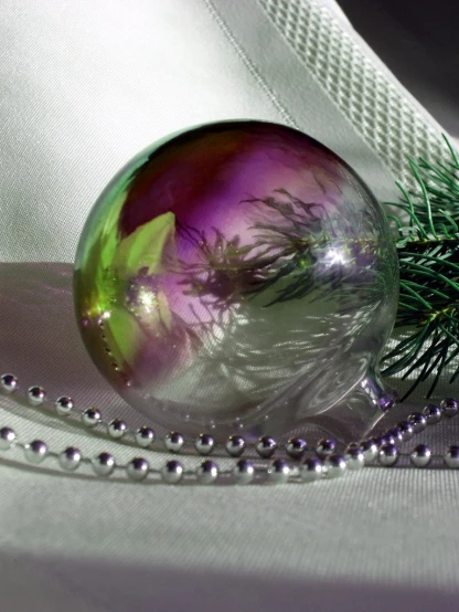 a glass ornament sitting on top of a bed with a pine tree nch