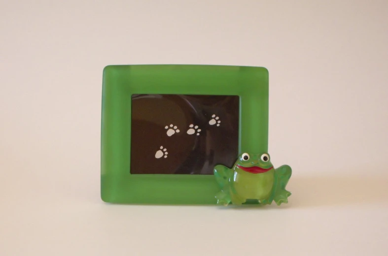 a toy frog next to a frame with paw prints on it