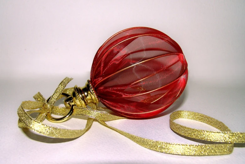 a red ornament wrapped in gold wire sitting on top of a white table