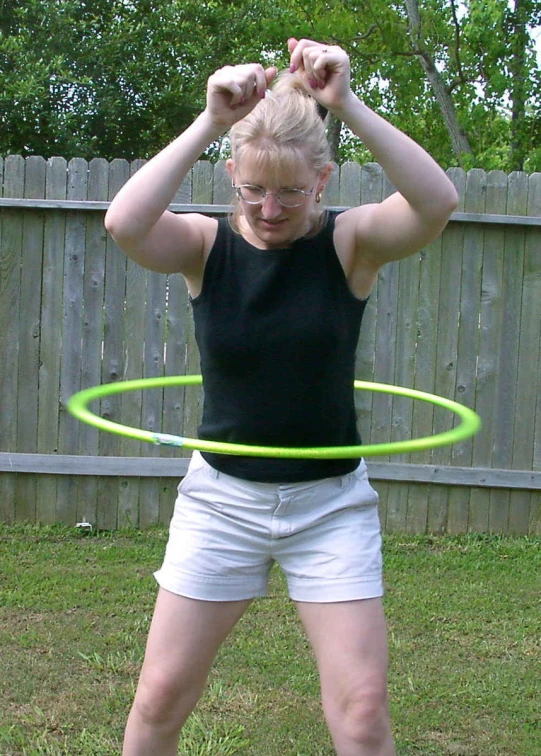 a woman is holding a neon green hula hoop in the backyard