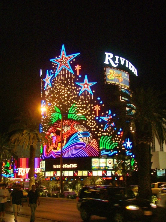 a night time view of an illuminated building and palm trees