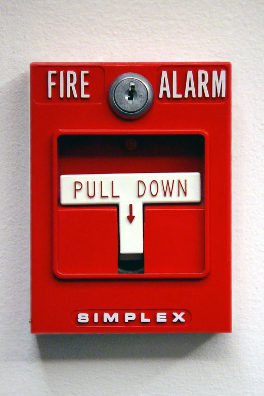 a red fire alarm on the wall in front of white walls