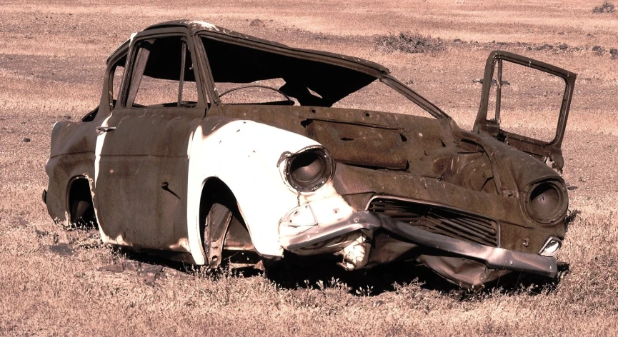 an old rusty car laying on top of a dry grass covered field