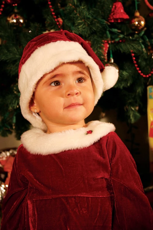 a little boy wearing a santa clause outfit in front of a christmas tree