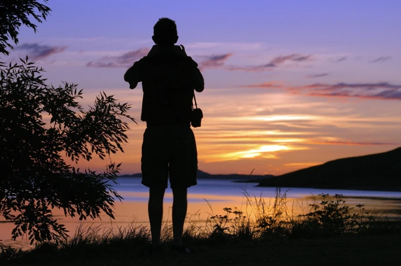 a person stands in front of the water at sunset