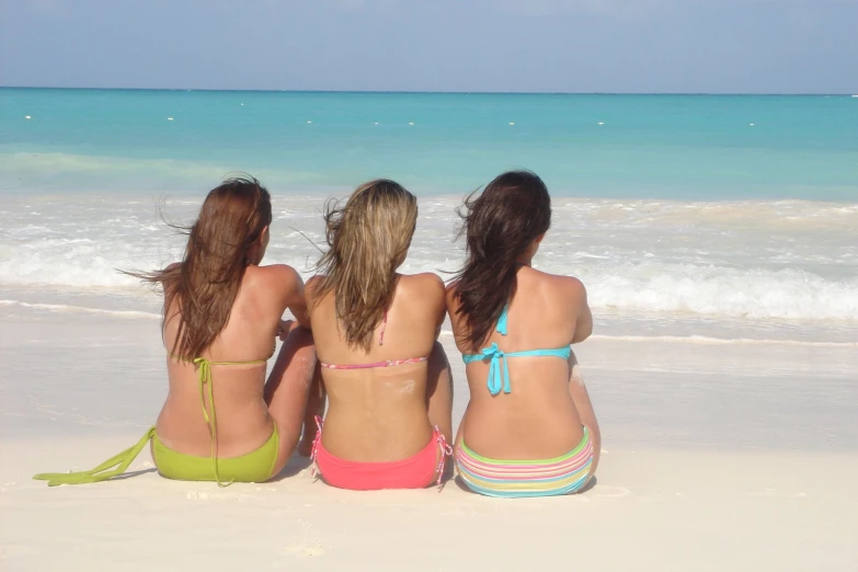 three girls in bikinis sit on the beach in front of the ocean