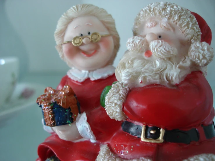 two plastic santa clauss are sitting together, one has a christmas cookie in his hand