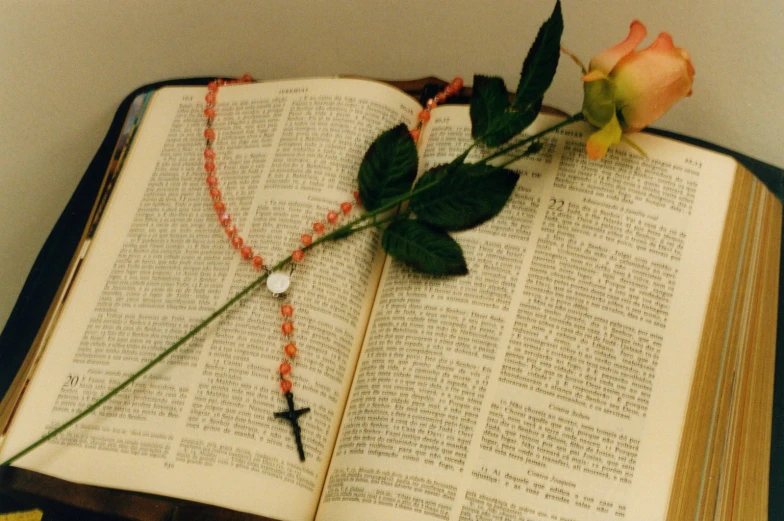 an open book on a table next to a rose and cross