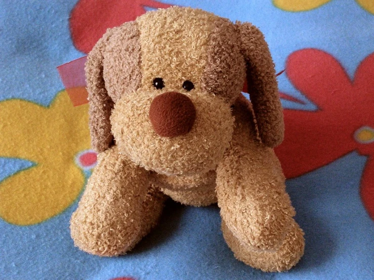 a small stuffed dog laying on a colorful patterned sheet