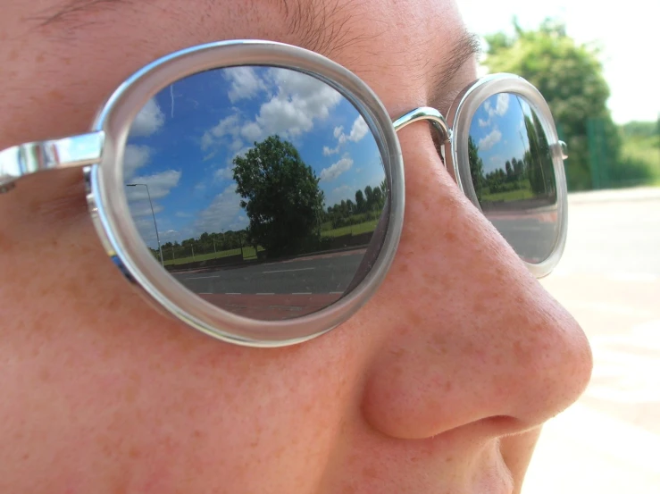 the reflection of trees in the mirrored circular sunglasses