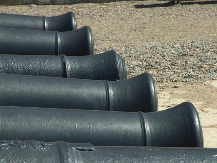 several black pipe lined up on a sand area