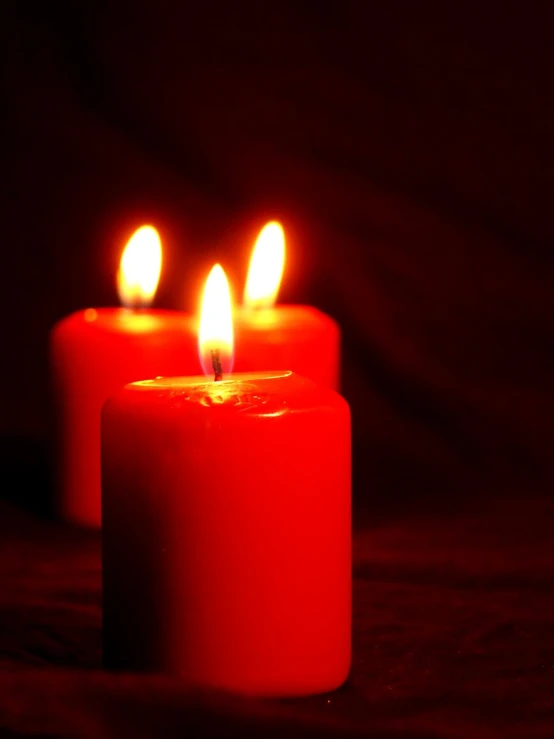 three lit candles glowing red in the dark