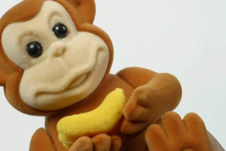 a stuffed monkey holding a small banana and wearing a yellow face