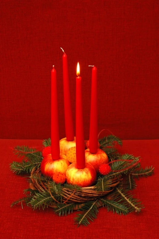 a group of red candles sitting next to apples and pine cones