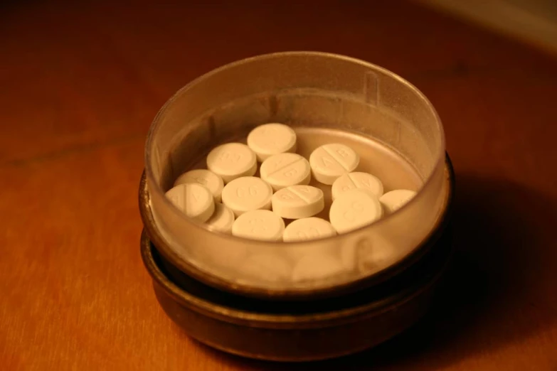 a metal container filled with white round pills on top of a wooden table