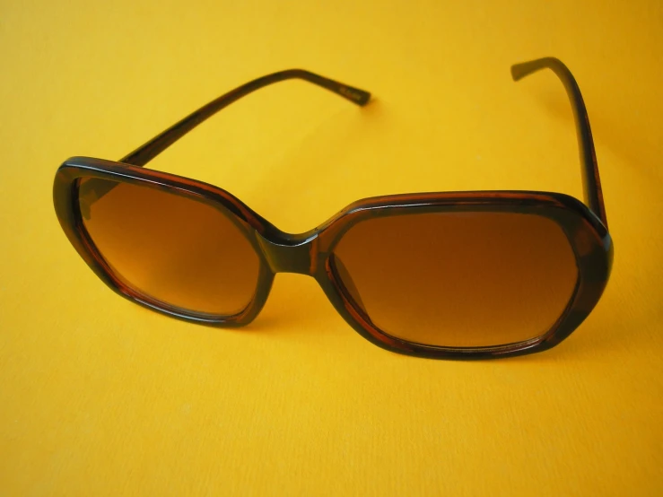 a sunglasses with brown tinted lenses on a yellow table