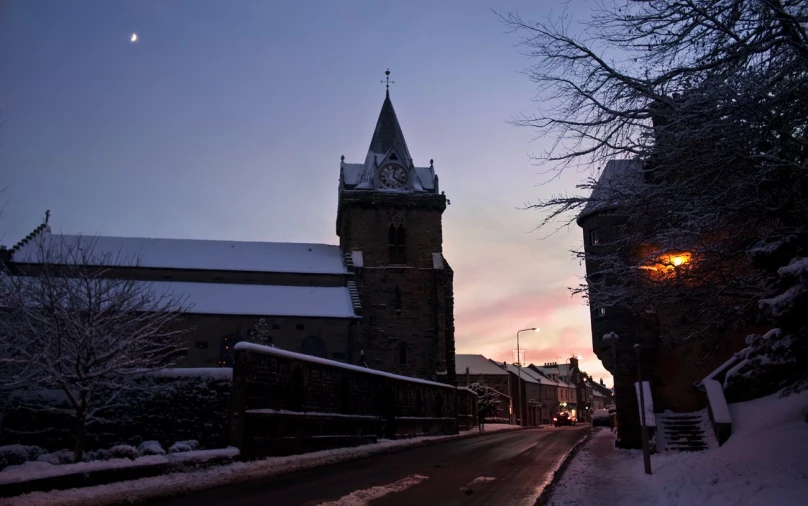 a snowy street with a large church at dusk