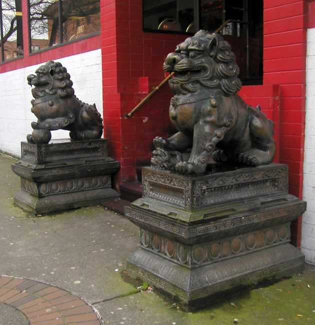 two statues of lions on cement bases in front of a red brick building