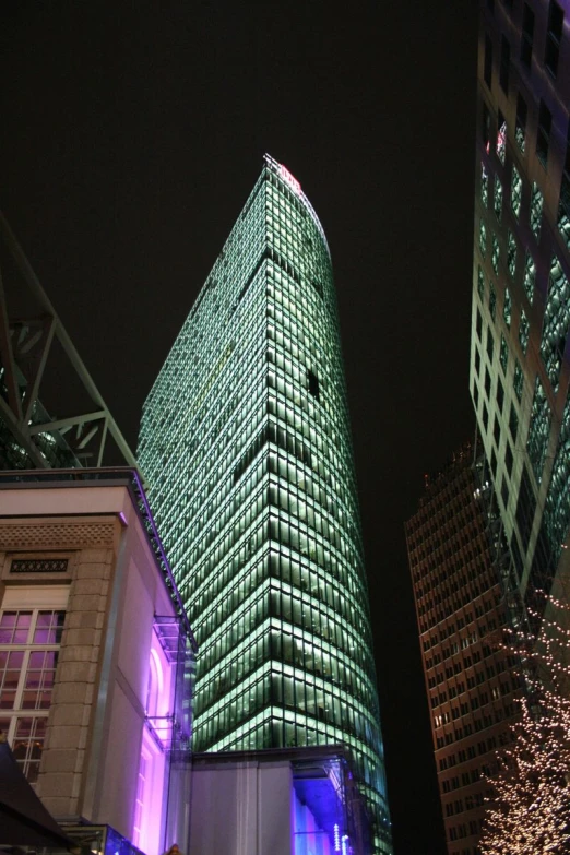 large green lighted skyscr at night with buildings in the background