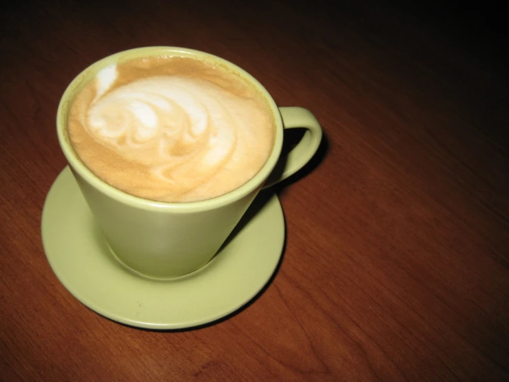 a green cup is on a saucer on a wooden table