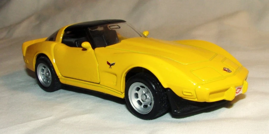 an yellow model car that is sitting on a white sheet