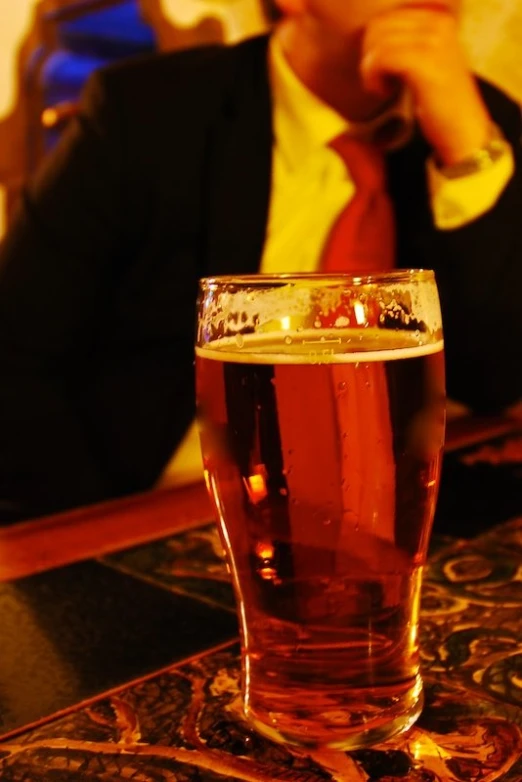 a man sitting in front of a tall glass filled with beer