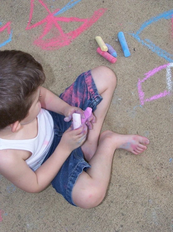 a young child sitting on the ground playing with chalk crayons