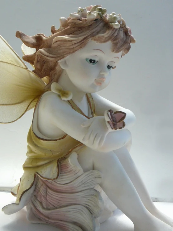 a fairy figurine holding a cupcake next to a white wall