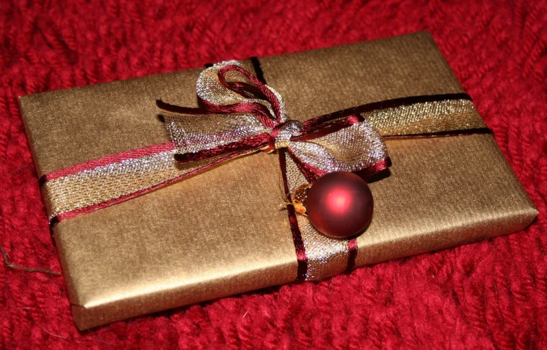 a present wrapped in gold paper with a red ornament