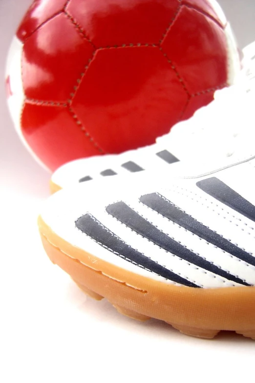 a red ball sitting next to a white and black soccer shoe