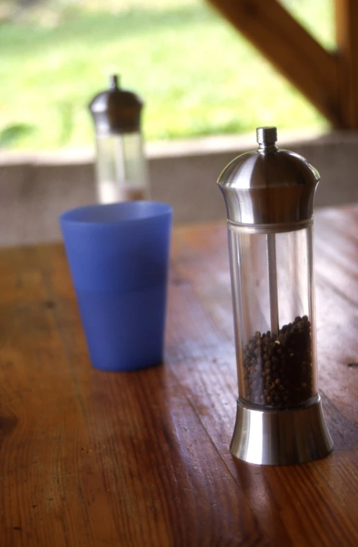 a metal coffee grinder with a blue cup in front of it