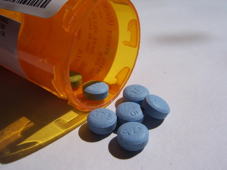 an orange prescription bottle next to two blue pills
