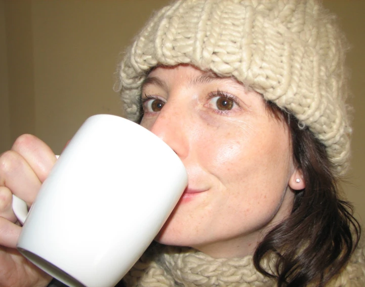 a girl wearing a white beanie drinking out of a mug