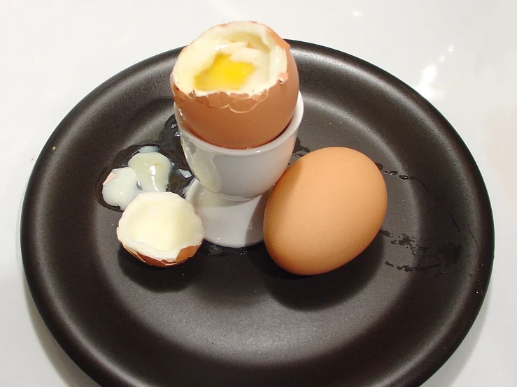 an egg sits in a small white cup next to a broken egg